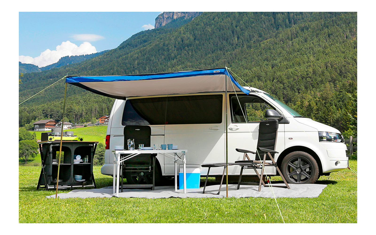 Wohnmobil mit ausgefahrener Markise, Campingstühle und Klapptisch im Grünen