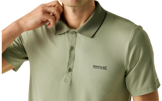 Porträt einer Person von der Brust aufwärts, trägt ein hellolivgrünes Poloshirt mit drei Knöpfen und kleinem Markenlogo auf der linken Brust; rechte Hand hält den Kragen; heller einfarbiger Hintergrund