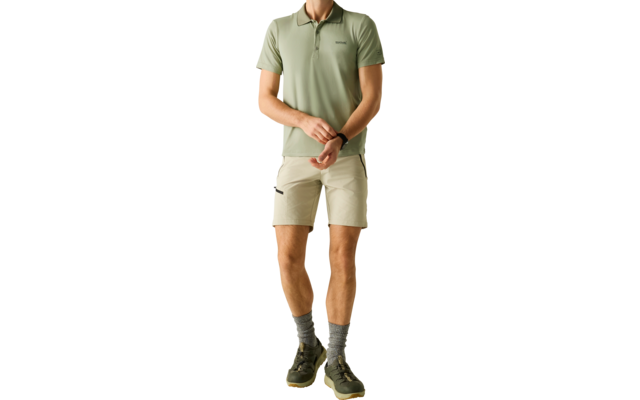 Mann steht vor hellem Hintergrund, trägt hellgrünes Polo, beige Shorts, graue Socken und grüne Sneaker; Hände vor dem Körper, Blick nach rechts