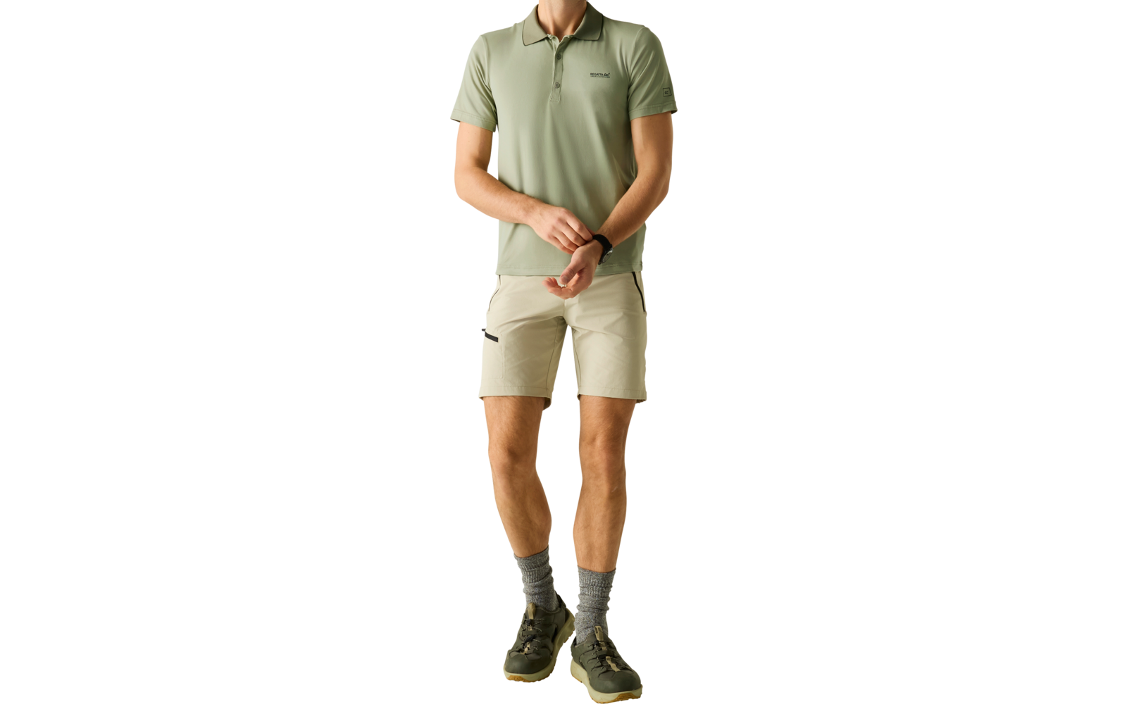 Mann steht vor hellem Hintergrund, trägt hellgrünes Polo, beige Shorts, graue Socken und grüne Sneaker; Hände vor dem Körper, Blick nach rechts