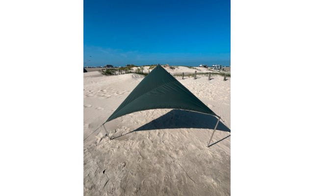 Dunkelgrünes, dreieckiges Tuch auf Metallstangen auf sandigem Strand, Schatten darunter, Dünen mit Gras und Gebäude im Hintergrund, blauer Himmel