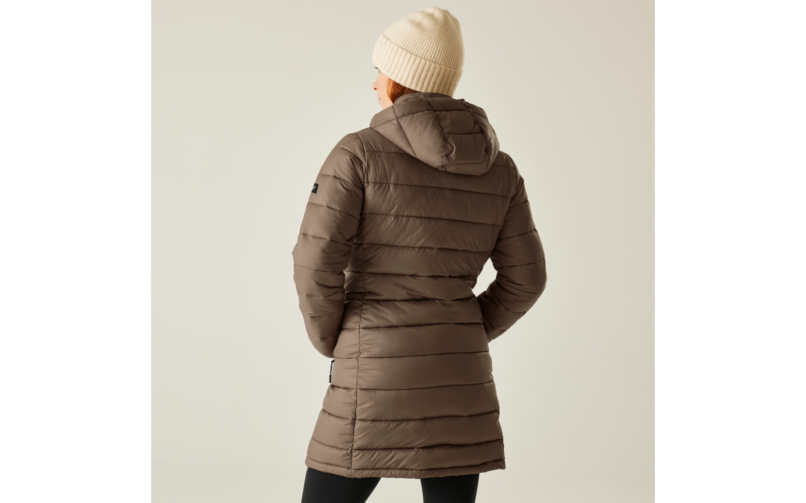 Person von hinten mit brauner Steppjacke und weißer Mütze vor hellem Hintergrund
