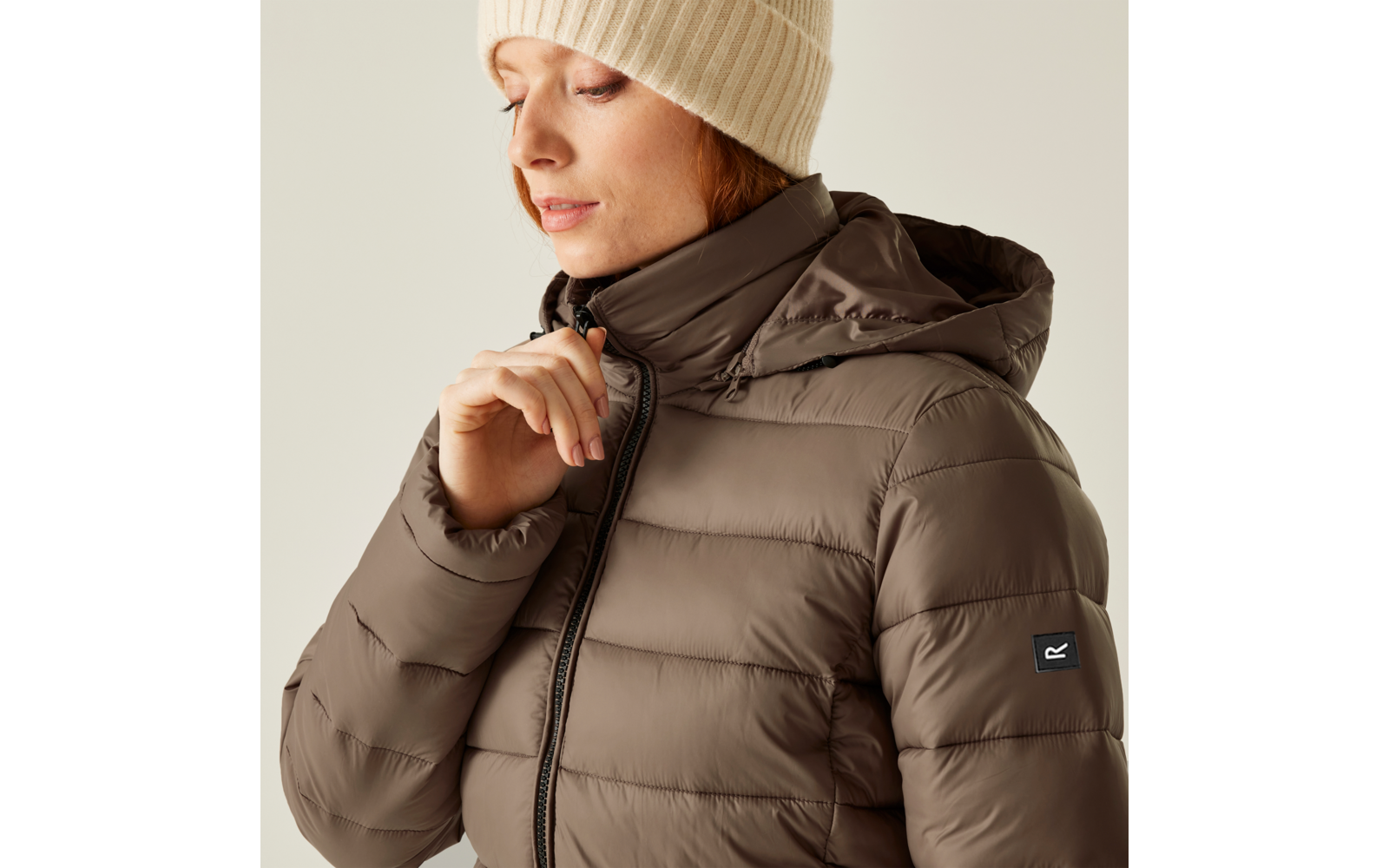 Frau in brauner Winterjacke und beige Mütze blickt nach unten
