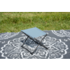 Tabouret pliant bleu clair sur une couverture grise à motif floral blanc sur de l'herbe verte