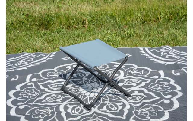 Tabouret pliant bleu clair sur une couverture grise à motif floral blanc sur de l'herbe verte
