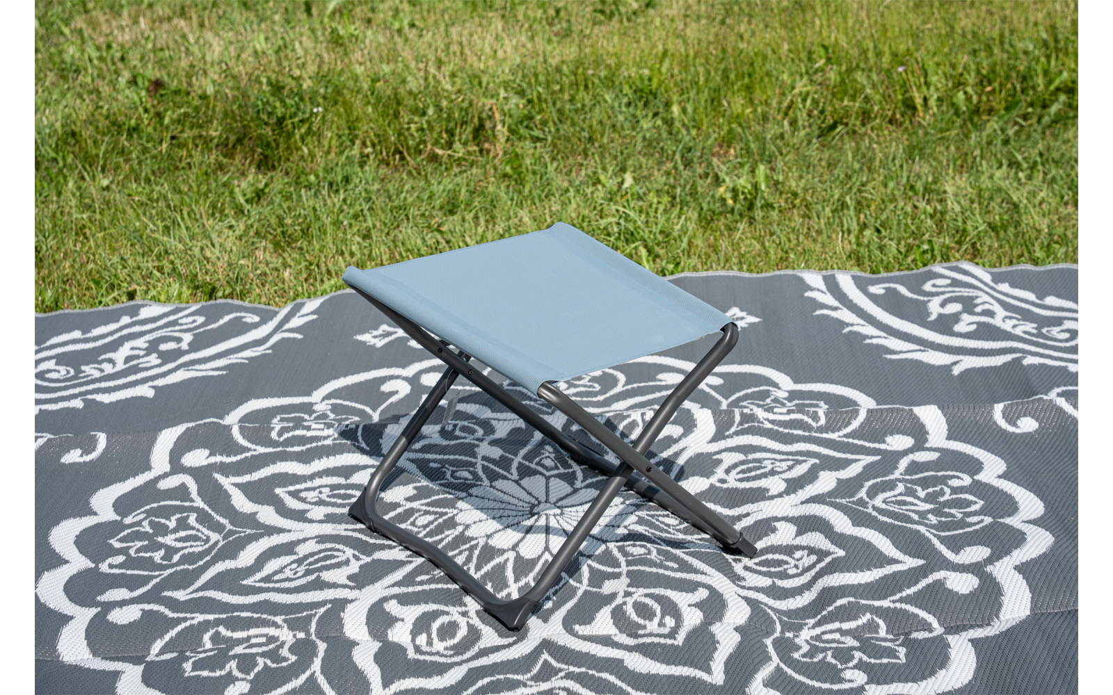 Tabouret pliant bleu clair sur une couverture grise à motif floral blanc sur de l'herbe verte