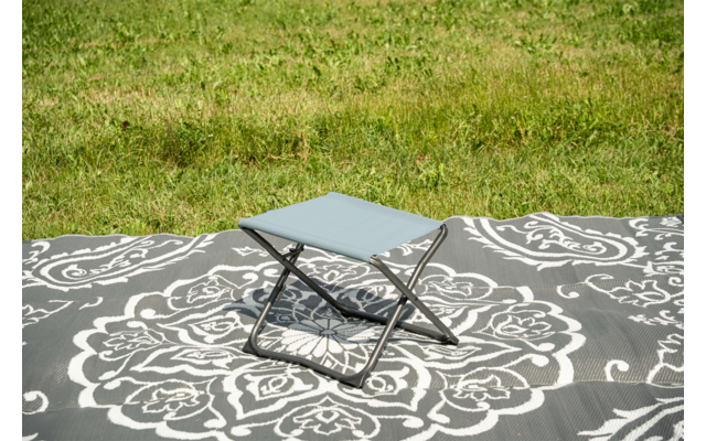 Petit tabouret pliant avec assise bleu clair sur une couverture à motif gris et blanc sur l'herbe