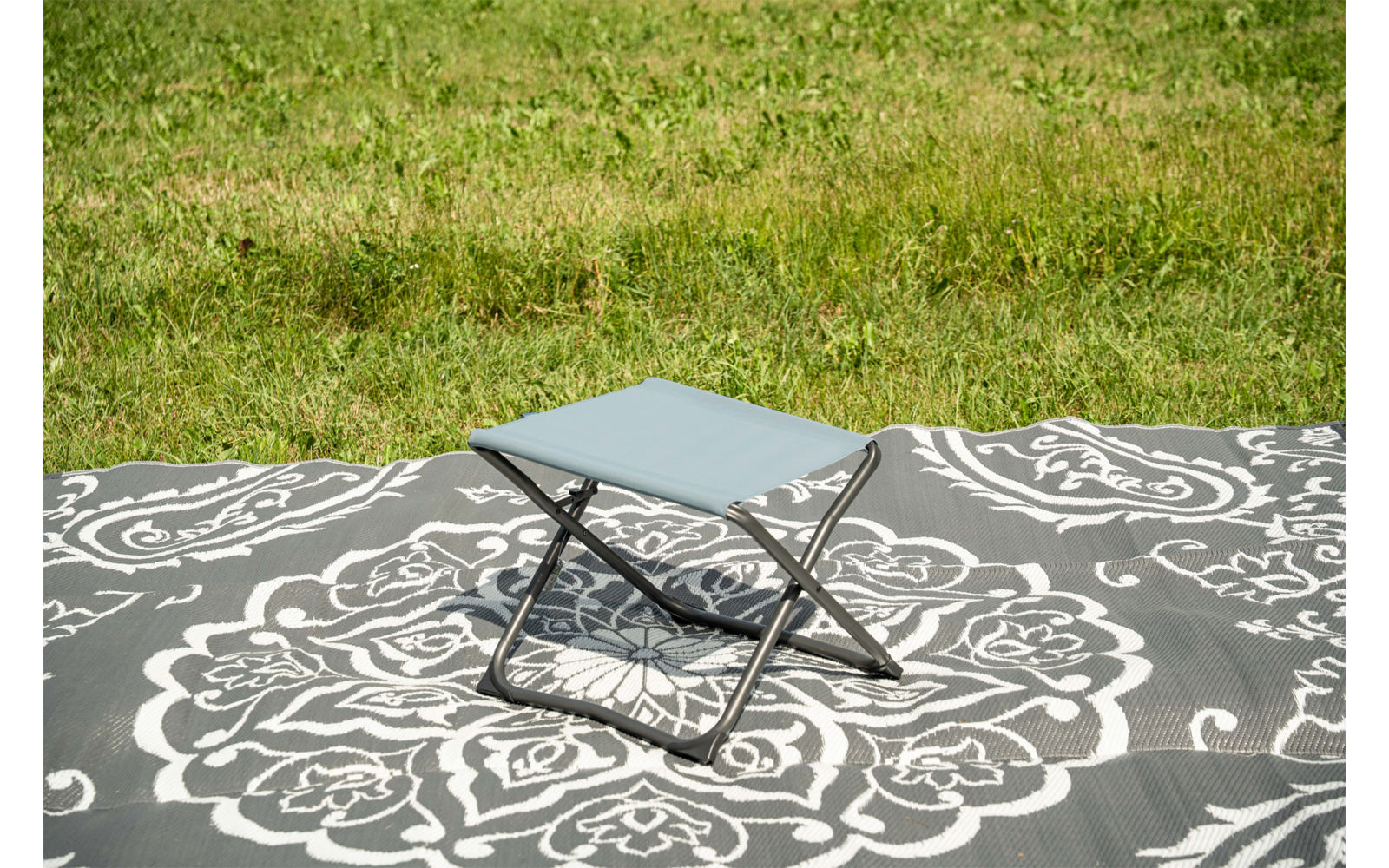 Petit tabouret pliant avec assise bleu clair sur une couverture à motif gris et blanc sur l'herbe
