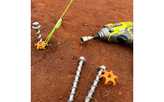 Gelber kabelloser Schrauber mit Steckaufsatz auf rotem Boden; drei spiralförmige Metallstangen; zwei orangefarbene sternförmige Kunststoffteile; neongrünes Seil, das an einer Stange befestigt ist