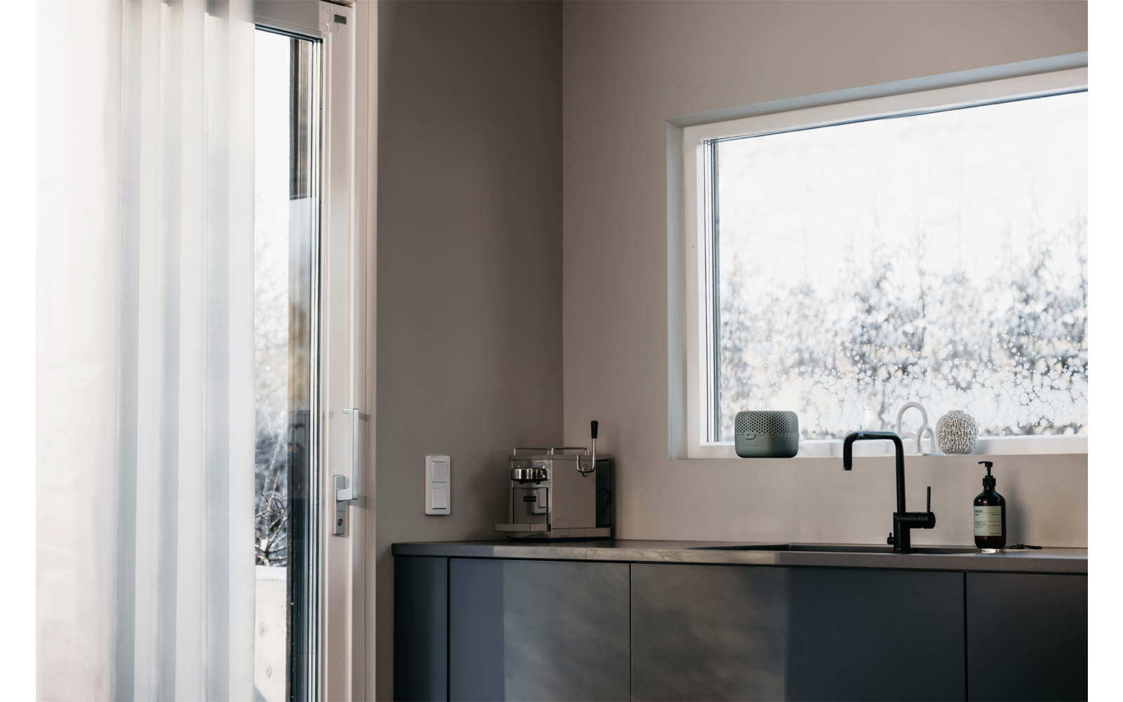 Moderner Küchenbereich mit schwarzer Arbeitsplatte, Wasserhahn und großem Fenster mit Blick ins Freie