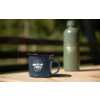 Tasse émaillée bleue avec inscription "camp life" sur une table en bois, thermos vert en arrière‑plan, clôture et arbres flous