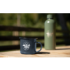 Blaue Emaille-Tasse mit Aufdruck "camp life" auf Holz­tisch, grüner Thermosbehälter im Hintergrund, unscharfer Zaun und Bäume
