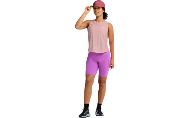 Person mit rosa Basecap, ärmellosem rosa Oberteil, hellvioletten Radshorts, schwarzen Socken und grauen Sportschuhen; stehend, eine Hand an der Cap-Krempe