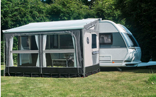 Caravane avec auvent attaché sur une pelouse devant des arbres
