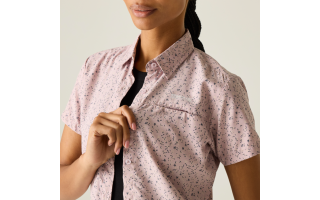 Person, Oberkörper von Schultern bis Brust sichtbar, trägt rosa kurzärmliges gemustertes Hemd über schwarzem Oberteil, eine Hand hält das Hemd an den Knöpfen, Zopf hinten, heller Hintergrund