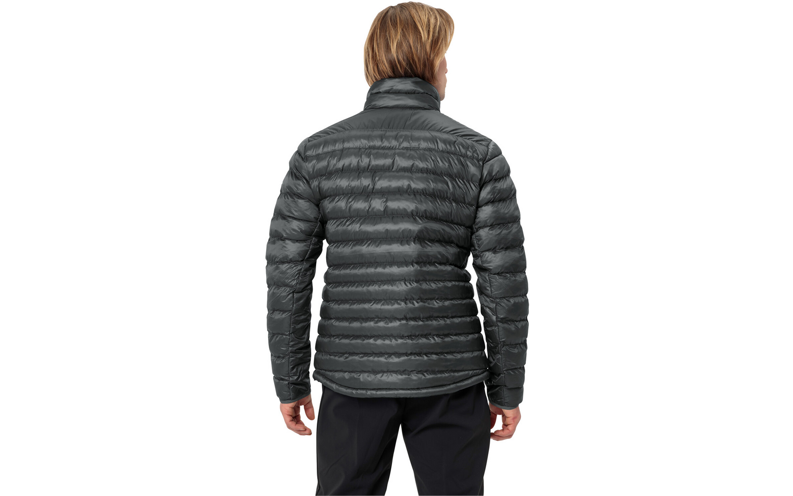 Person von hinten, trägt dunkelgraue gesteppte Jacke mit horizontalen Nähten und dunkle Hosen; kurzes hellbraunes Haar; weißer Hintergrund