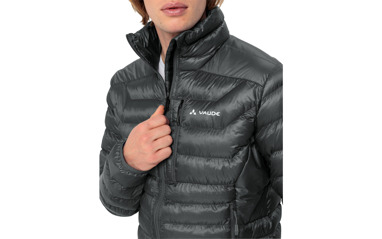 Oberkörper einer Person in dunkler, gesteppten Pufferjacke mit Vaude-Logo, Hand hält den Reißverschluss, weißes T-Shirt sichtbar