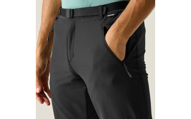 Unterer Rumpf einer Person: hellblaues Oberteil, schwarze Hose mit Gürtel; rechte Hand in vorderer Hosentasche, linker Arm an der Seite, Reißverschlusstasche sichtbar