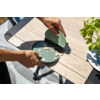 Deux mains balaient des miettes avec une petite brosse dans une coupelle sur une table en bois claire ; plante en pot à droite