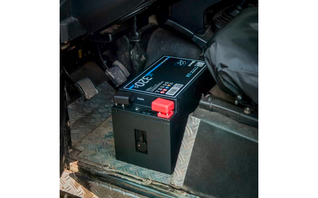 Schwarze Autobatterie in Fahrzeuginnenraum mit roten und blauen Kabelanschlüssen