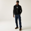 Mann in schwarzer Jacke, blauer Jeans und braunen Schuhen steht vor heller Wand