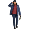 Persona caminando, lleva chaqueta azul marino, camiseta roja, pantalones azul marino, gorro y zapatos negros, sostiene una botella de agua en la mano derecha