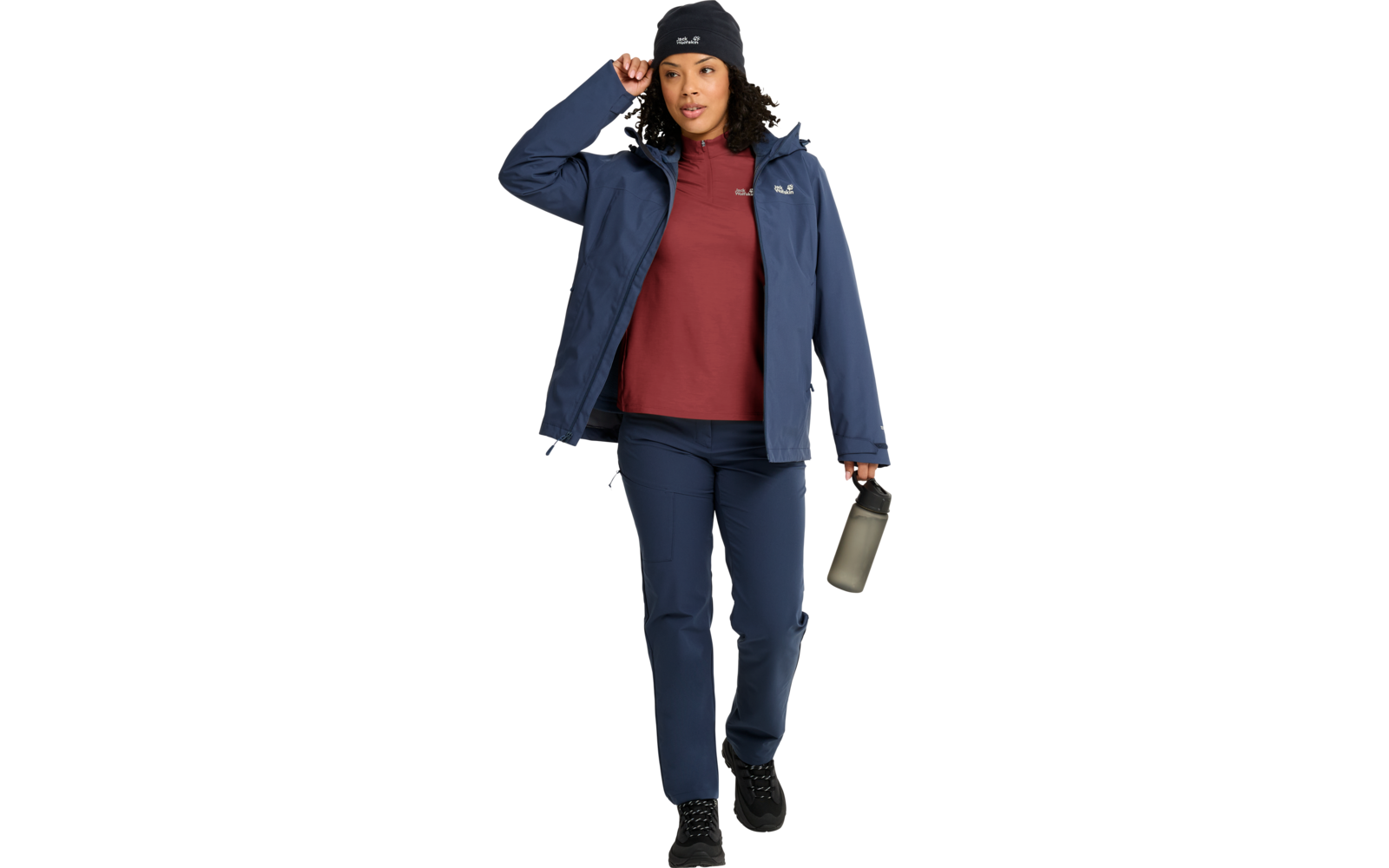 Persona caminando, lleva chaqueta azul marino, camiseta roja, pantalones azul marino, gorro y zapatos negros, sostiene una botella de agua en la mano derecha