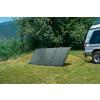 Drei Solarplatten stehen auf dem Boden neben einem weißen Auto auf einer grünen Wiese