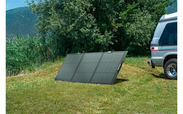 Drei Solarplatten stehen auf dem Boden neben einem weißen Auto auf einer grünen Wiese