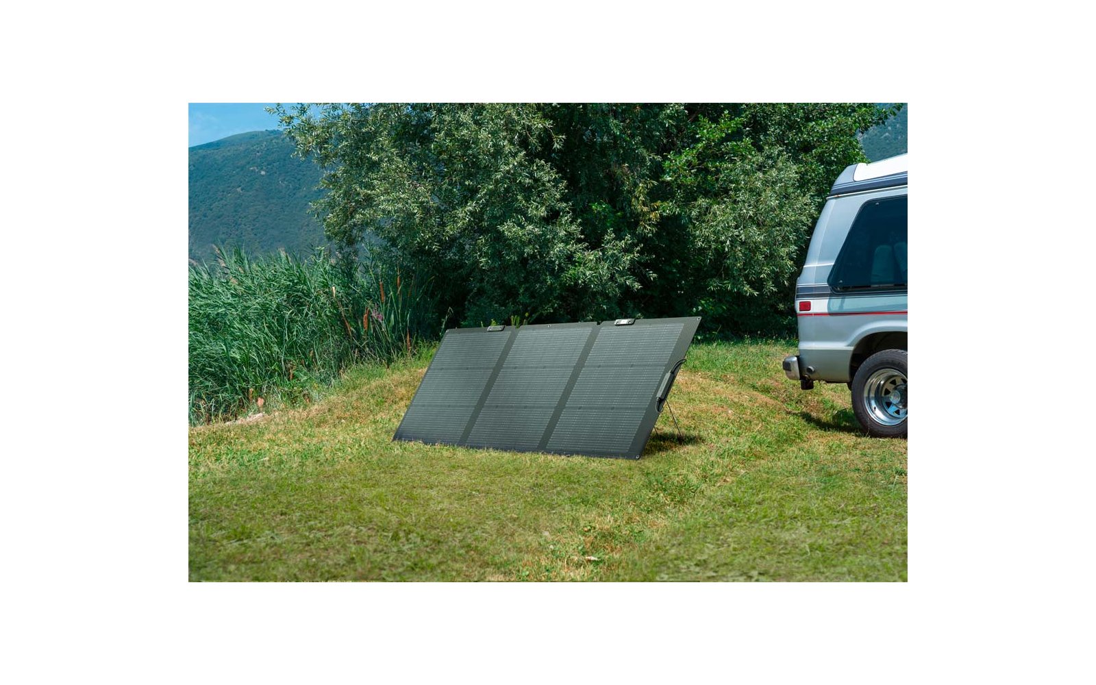 Drei Solarplatten stehen auf dem Boden neben einem weißen Auto auf einer grünen Wiese
