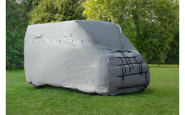 Gray cover drapes over a vehicle on green grass in front of trees