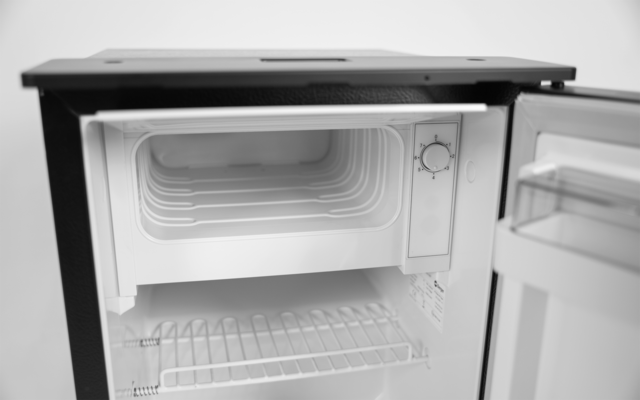 Offener Minikühlschrank mit kleinem Gefrierfach oben, Drahtablage, Türfach und Temperaturregler an der rechten Innenwand