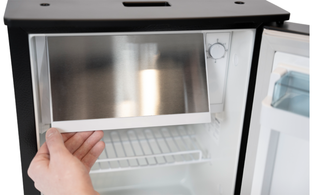 Hand zieht ein herausnehmbares Fach aus dem oberen Bereich eines kleinen offenen Kühlschranks