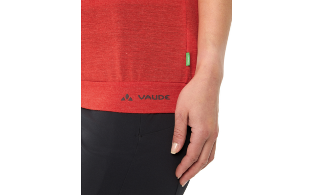 Bas d'un t‑shirt rouge avec logo noir VAUDE à l'ourlet, petite étiquette latérale verte, main droite sur la hanche, pantalon noir