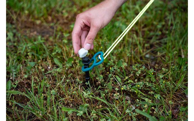 Hand hält weißes Kunststoffteil an blauem Hering mit neon-gelber Leine im Gras