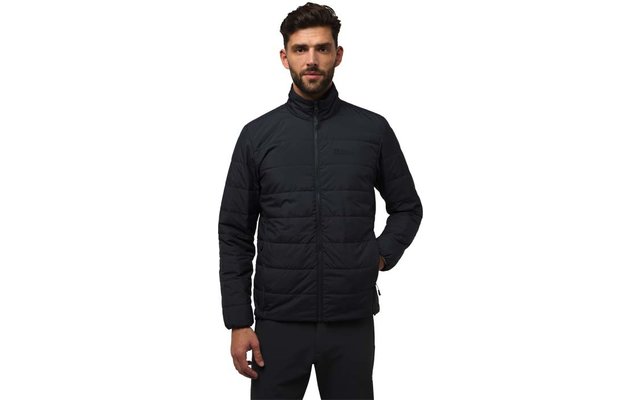 Homme aux cheveux courts et foncés et barbe portant une veste matelassée noire à col montant, mains dans les poches, debout devant un fond blanc