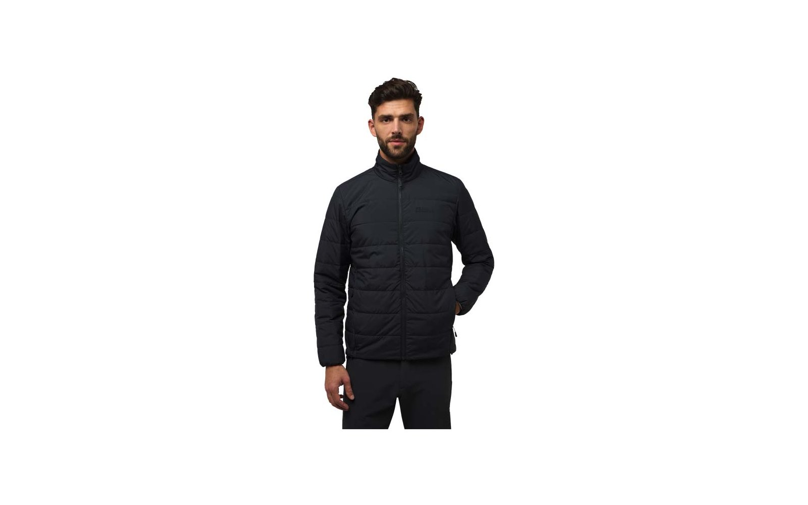 Homme aux cheveux courts et foncés et barbe portant une veste matelassée noire à col montant, mains dans les poches, debout devant un fond blanc