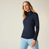 Femme aux longs cheveux blonds portant un pull bleu foncé et un pantalon bleu clair devant un fond clair