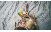 Kind und Erwachsener lesen zusammen ein Bilderbuch auf einer grauen Decke