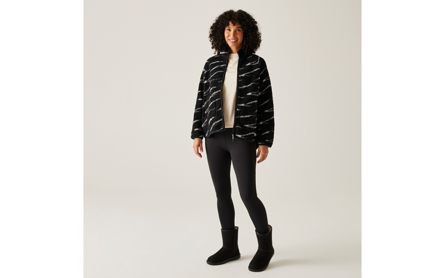 Frau trägt schwarze gesteppte Jacke, weiße Bluse, schwarze Leggings und schwarze Stiefel
