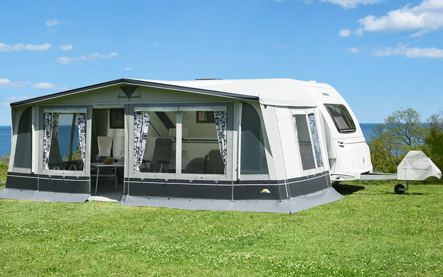 Una caravana con una tienda adjunta en un césped verde bajo un cielo azul con nubes