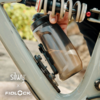 Hand, die eine transluzente Trinkflasche in einen am grauen Fahrradrahmen montierten Flaschenhalter steckt; Fahrradfeder und Logos 'silwy x FIDLOCK' sichtbar