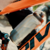 Nahaufnahme eines orangefarbenen Fahrradrahmens mit einer silbernen Trinkflasche mit schwarzem Verschluss in einem Flaschenhalter