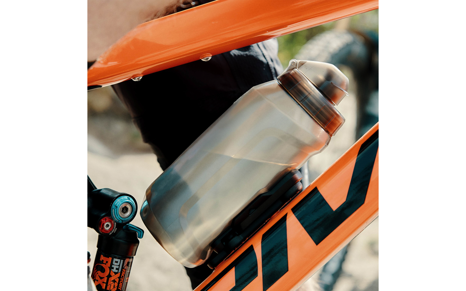 Nahaufnahme eines orangefarbenen Fahrradrahmens mit einer silbernen Trinkflasche mit schwarzem Verschluss in einem Flaschenhalter