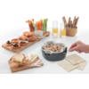 Tisch mit verschiedenen Snacks, darunter Brot, Aufstriche, Nüsse, Getränke und eine Hand, die einen Löffel hält