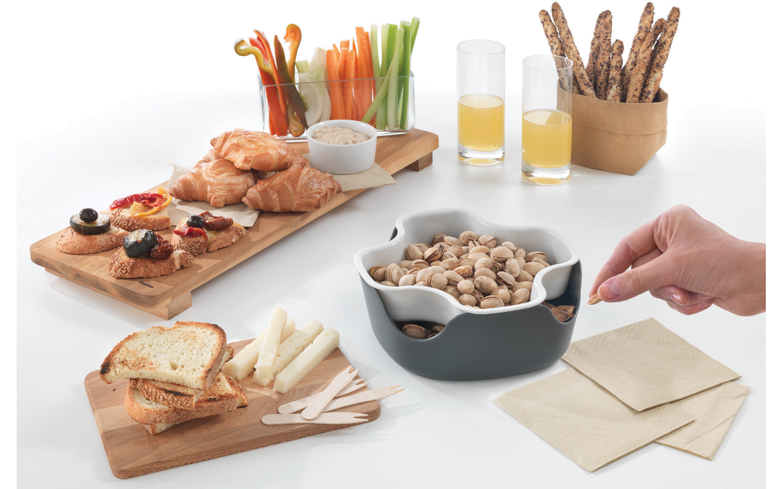 Tisch mit verschiedenen Snacks, darunter Brot, Aufstriche, Nüsse, Getränke und eine Hand, die einen Löffel hält