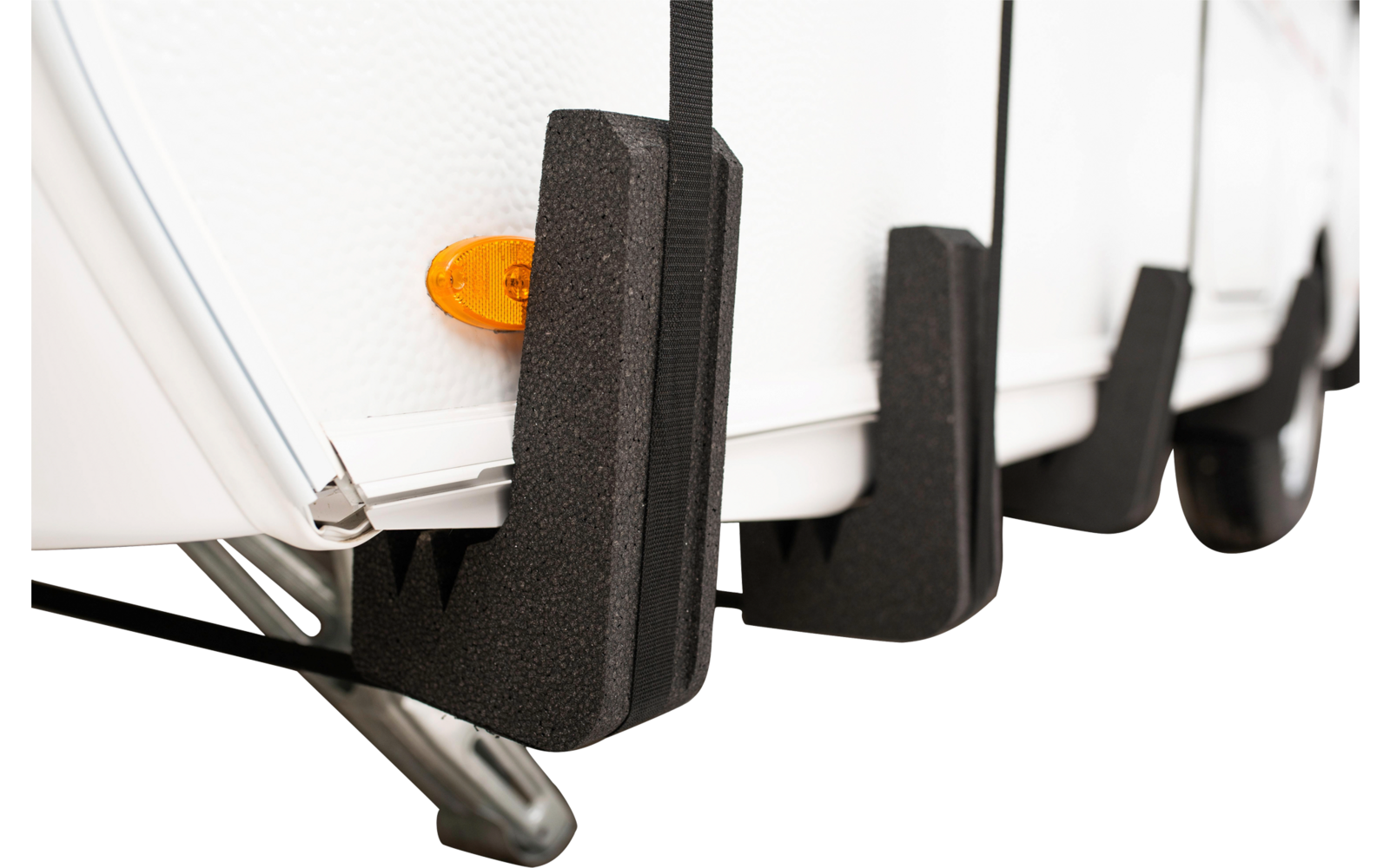 Untere Kante einer weißen Seitenwand mit orangefarbenem Reflektor, schwarzen Schaumstoffkeilen an der Unterseite und einer sichtbaren Metallstütze