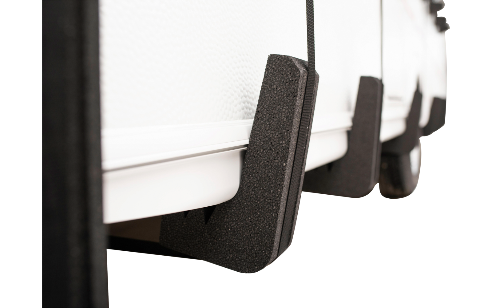 Nahaufnahme schwarzer Schaumstoffstücke an der Unterkante eines weißen, gerippten Objekts; mehrere in Reihe, unscharfer Hintergrund