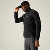 Person mit schwarzer Baseballkappe und schwarzem Reißverschluss-Pullover, hebt die rechte Hand an die Kappe, in Dreiviertelansicht vor hellem Hintergrund