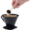 Main tenant une cuillère doseuse blanche de café moulu au-dessus d'un porte-filtre conique noir avec filtre en papier sur fond blanc